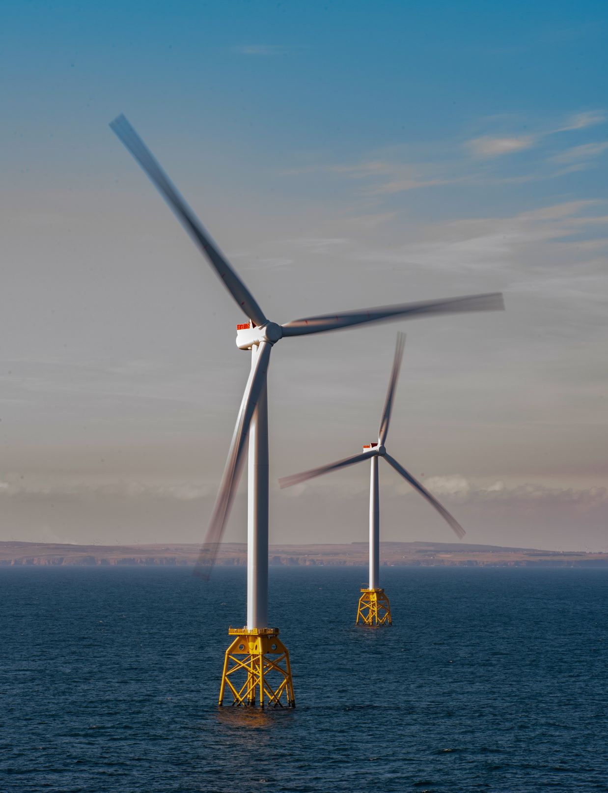 Two offshore wind turbines moving creating a slightly blurred image of them out at sea